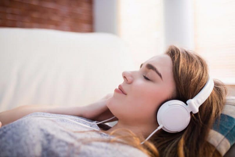 A girl listening to learn self-hypnosis through white headphones with her eyes closed