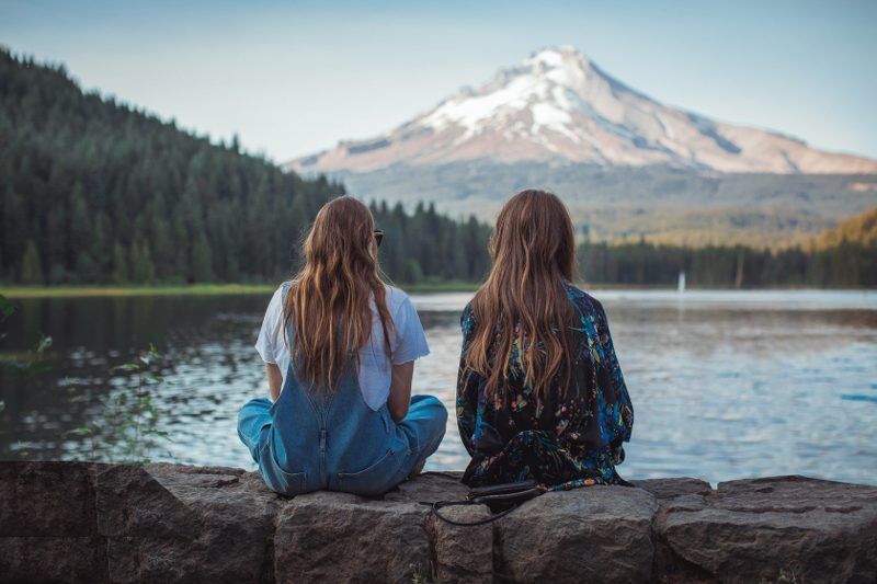 Two female friends sitting in front of a lake to listen to understand each other. 